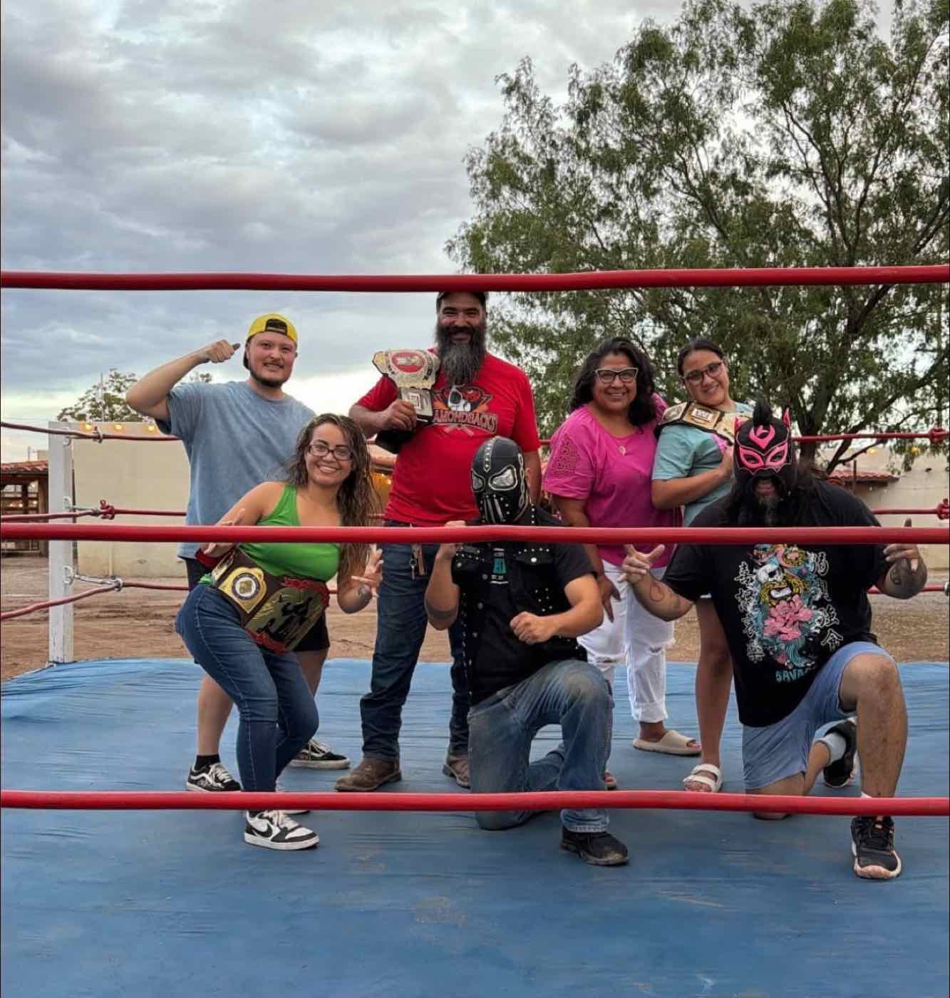 Supporters posing in a wrestling ring with masked luchadores and championship belts at Three Missions Brewery